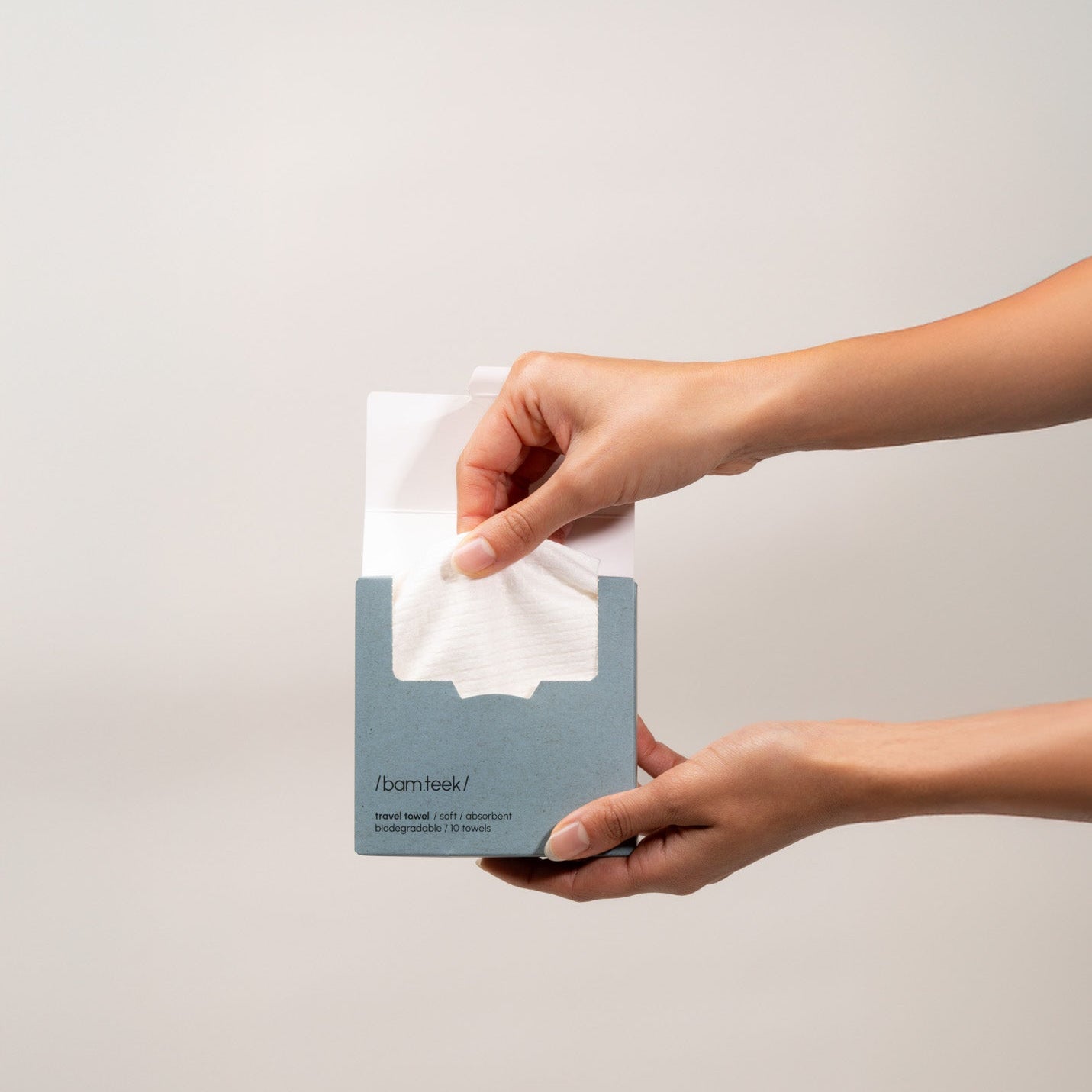 Hands holding a single-use travel towel from the Travel Bundle, designed for clean skincare on the go.