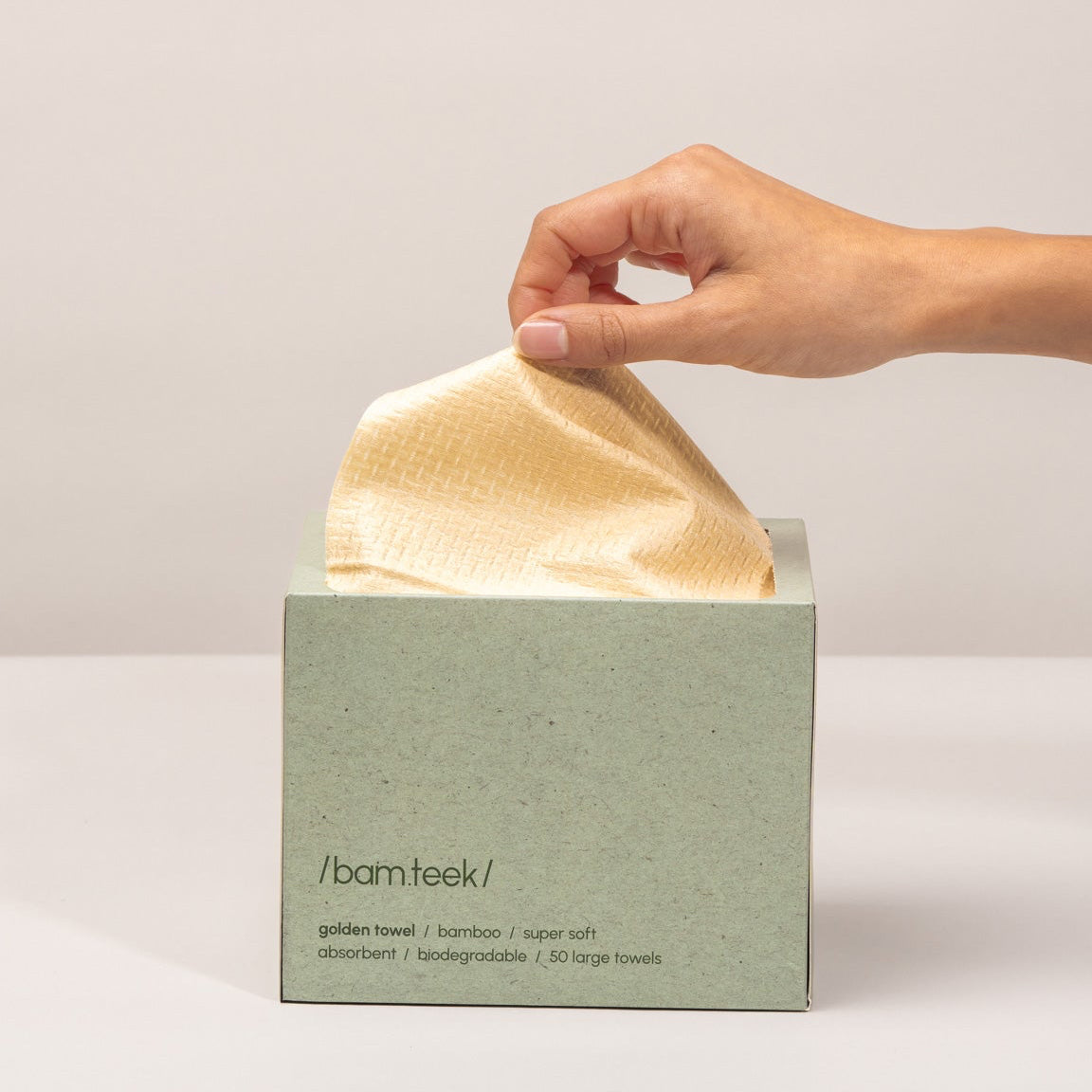 A hand retrieving a soft gold bamboo towel from a stylish box of Golden Pack by bamteek.