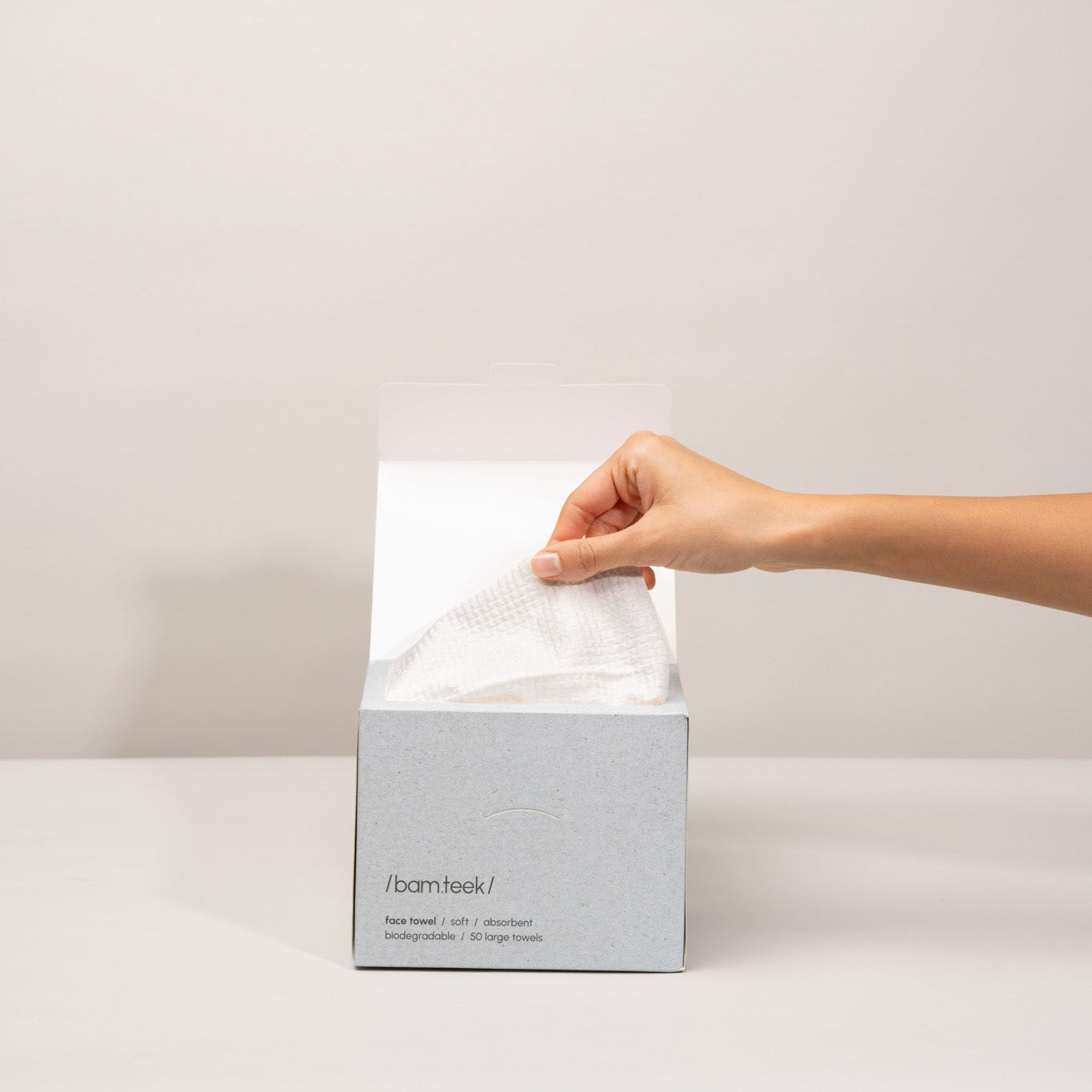 Hand reaching into Bamteek box to pull out a single-use face towel for skincare. Hand reaching into Bamteek box to pull out a single-use face towel for skincare.